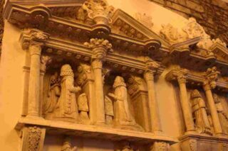 A stone memorial mounted on the walls of St Audoen's A couple kneel in prayer facing each other. Symbolic carvings surrounding them include baskets of pomegranates featured prominently above the deceased at prayer.
