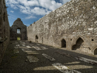 the internal, roofless, structure of the abbey, with flat gravestones marked across the gravel ground